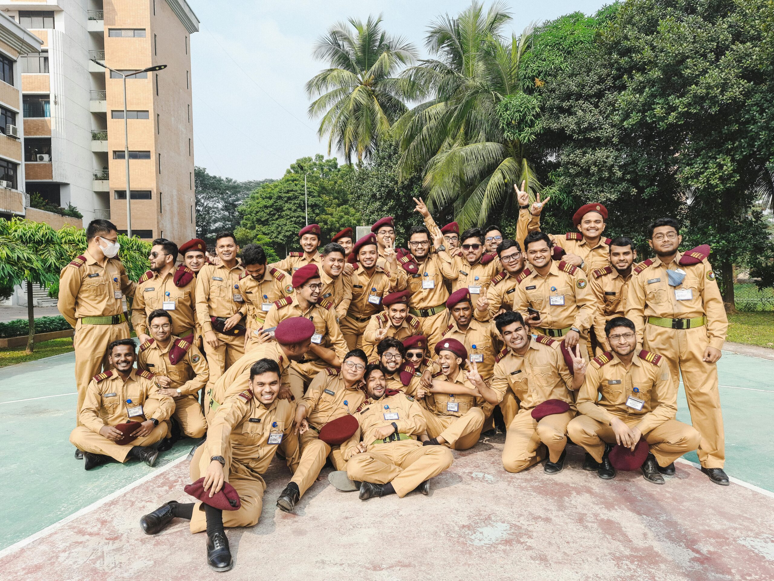 A large group of young soldiers in uniform happily posing together outdoors in Dhaka, Bangladesh.
