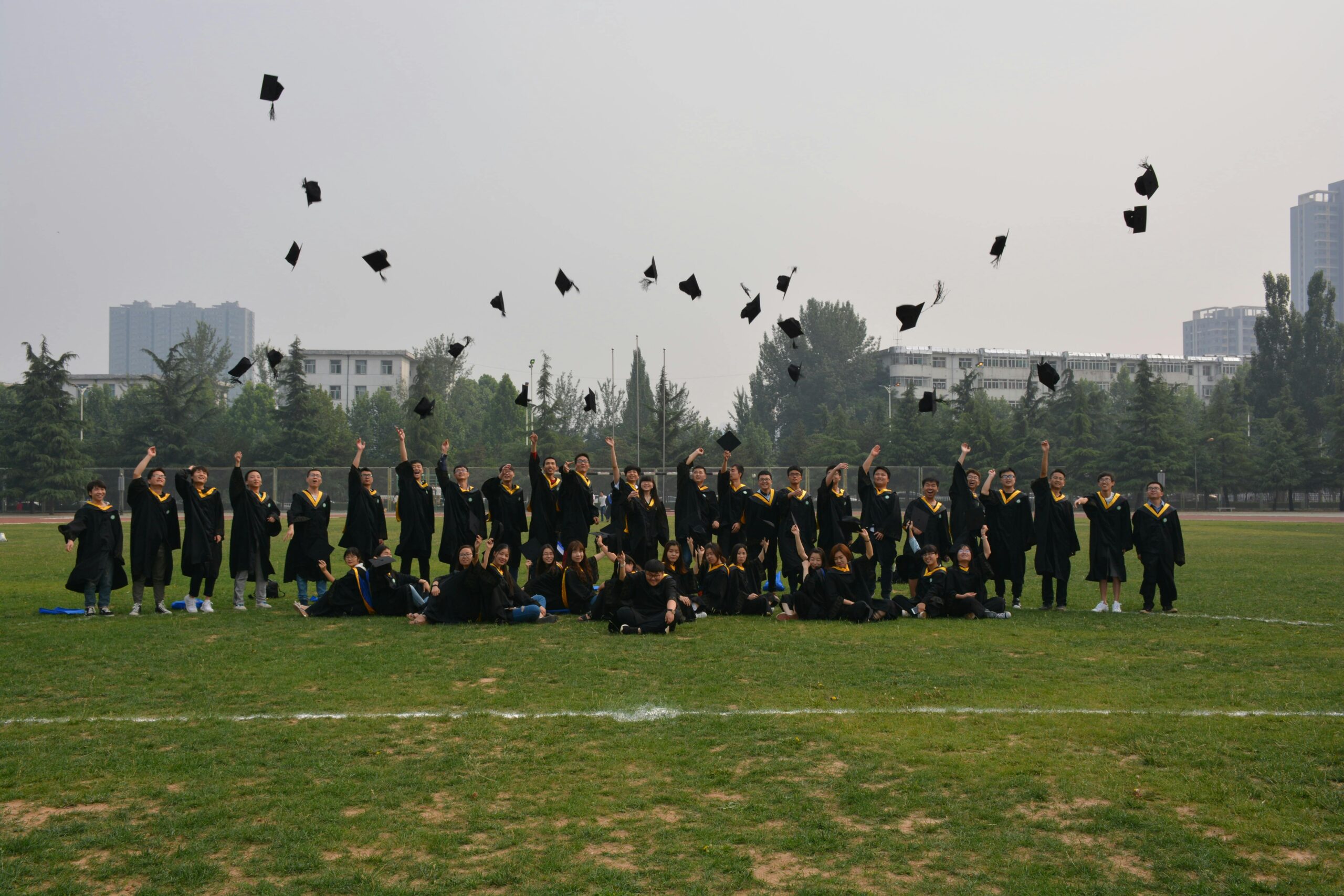 A large group of graduates celebrating by tossing their caps in the air outdoors.